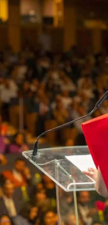 Alumna de master de espaldas hablando al público en graduación
